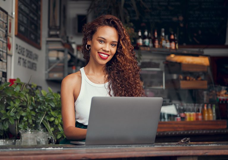 Woman sat at a laptop smiling having read our blog post about how to Drive More Traffic to Your Blog