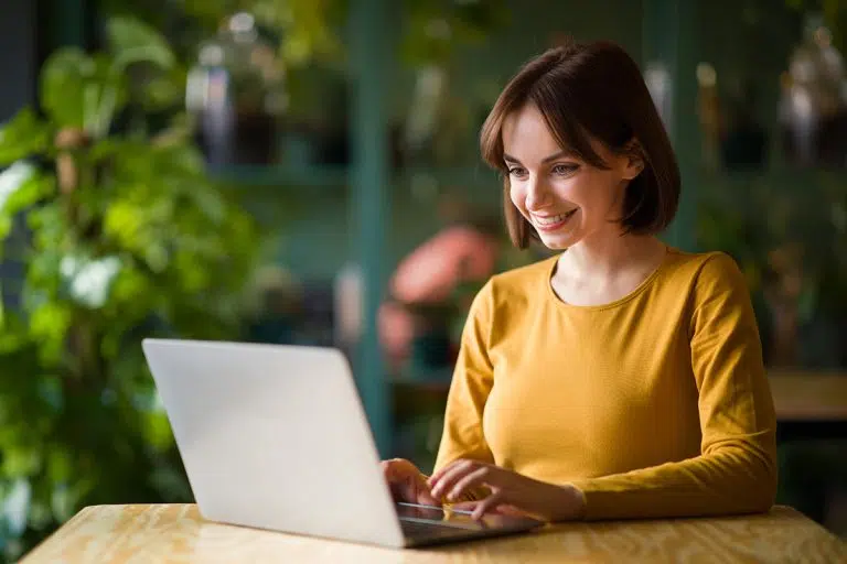 Woman smiling while writing at her computer having learnt the benefits of blogging